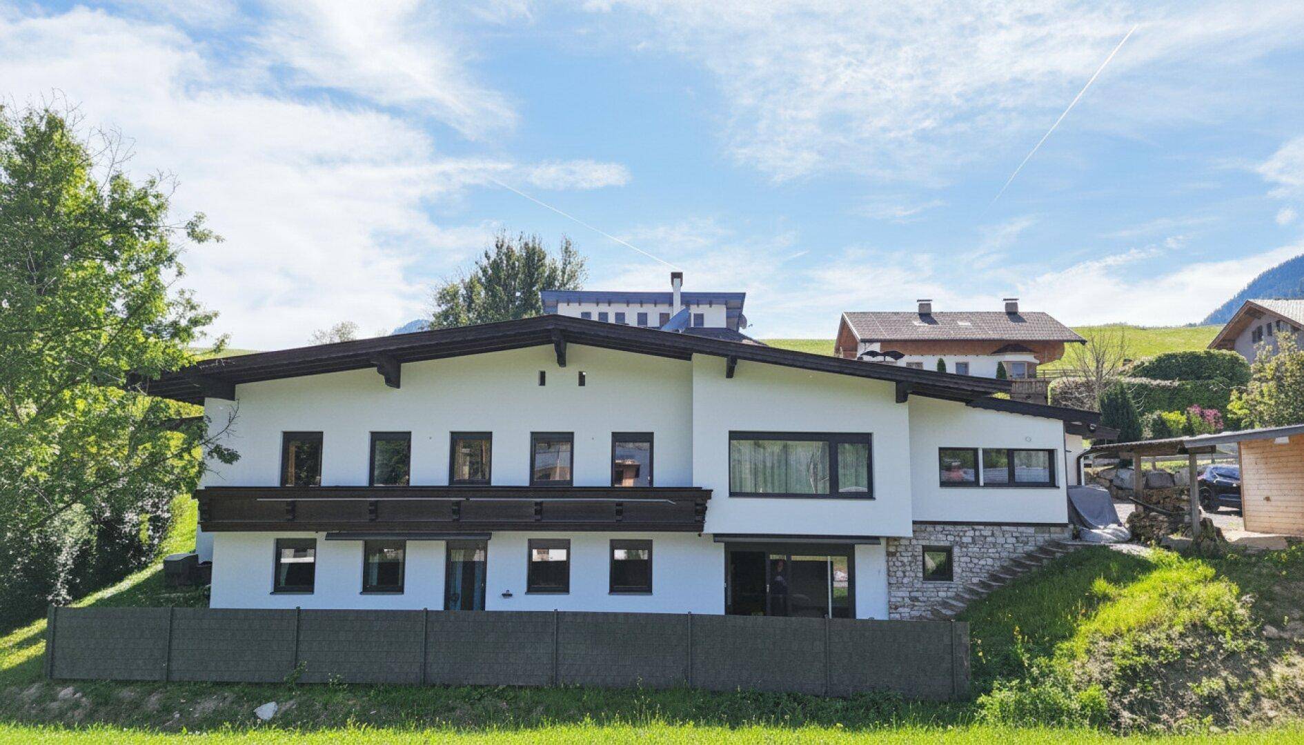 Ansicht des Hauses mit moderner Fassade, Balkonen und grüner Umgebung unter blauem Himmel.