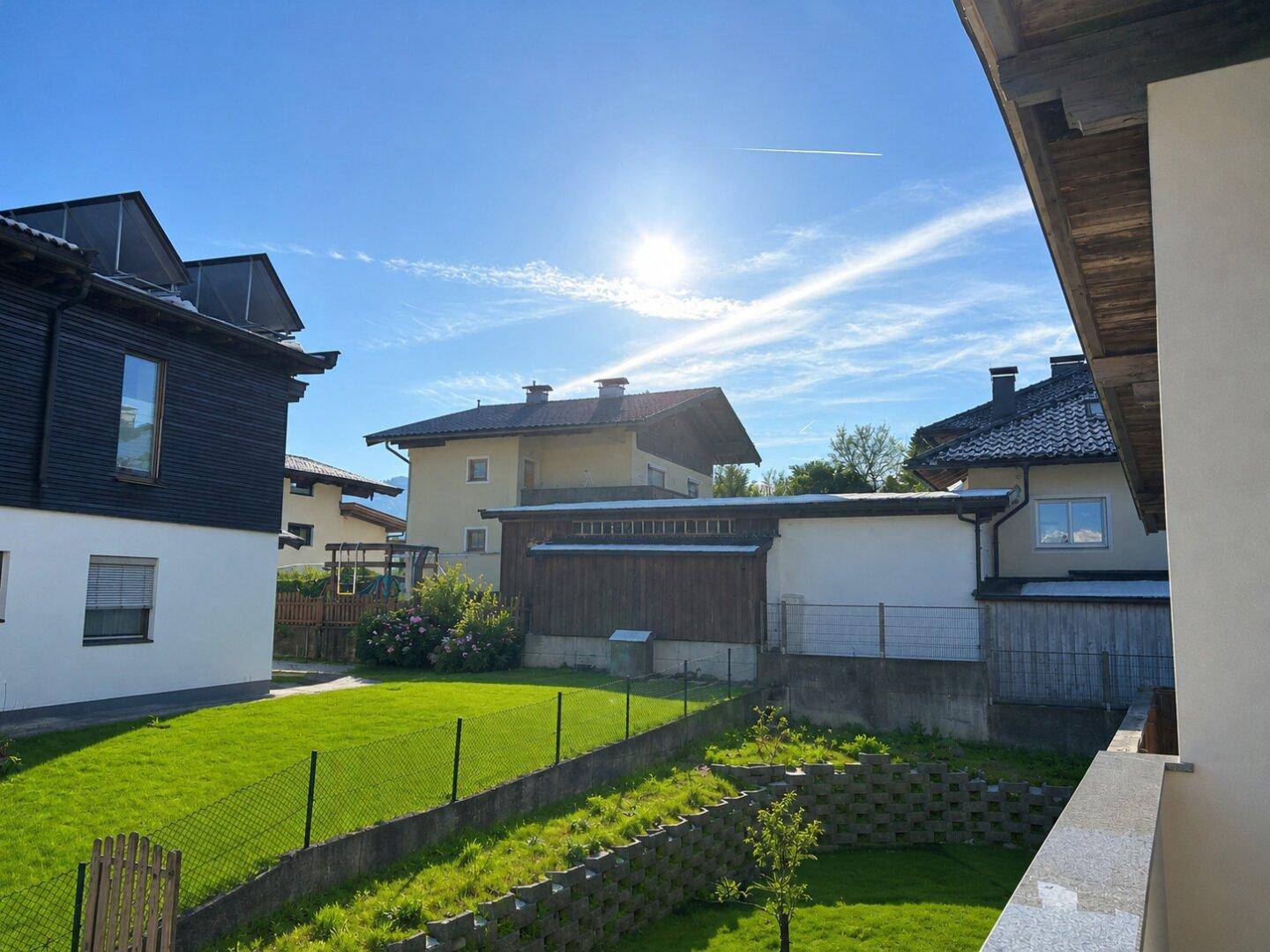 Sonniger Ausblick auf den grünen Gartenbereich und die umliegenden Häuser mit blauem Himmel.