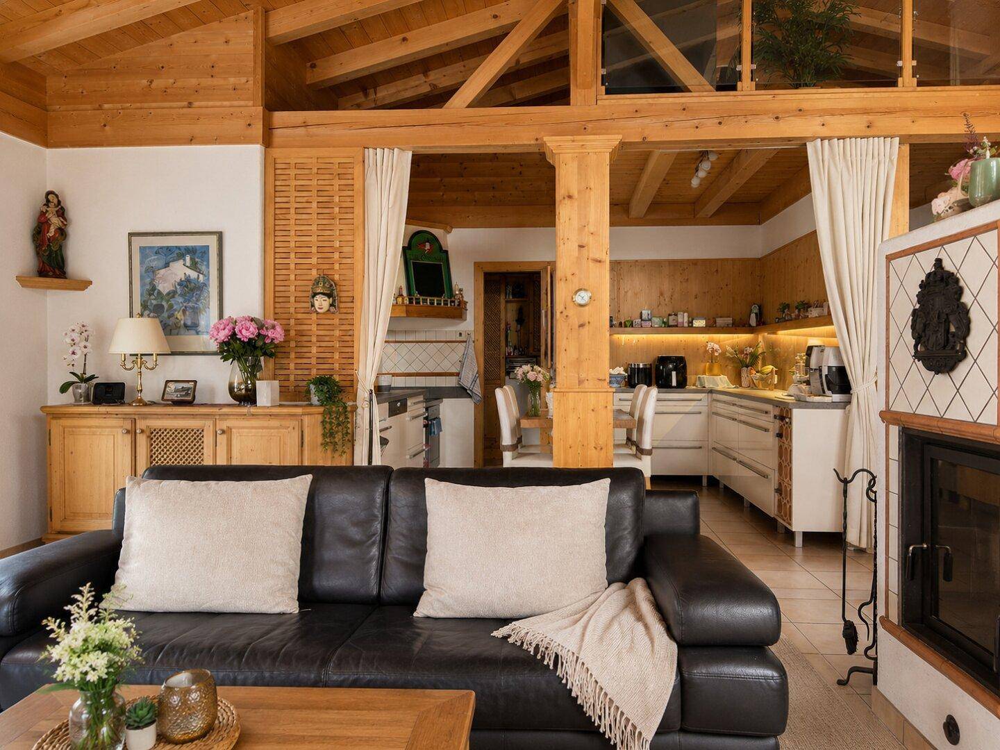 Gemütlicher offener Wohnbereich mit Holzbalkendecke, Kamin und integrierter Küche im Landhausstil.