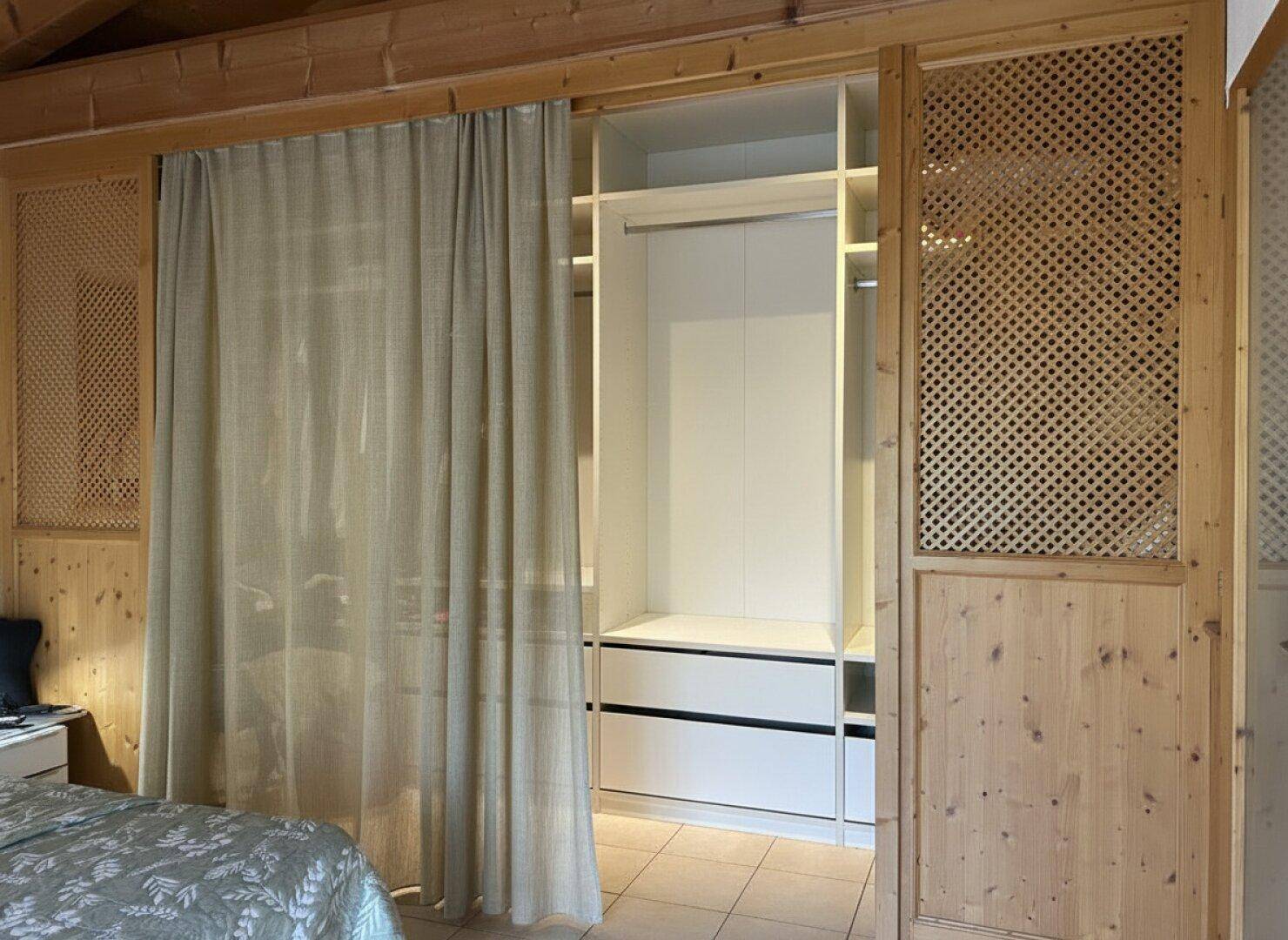 Integrierter Kleiderschrank mit offenen Fächern und Vorhang in einem Schlafzimmer.