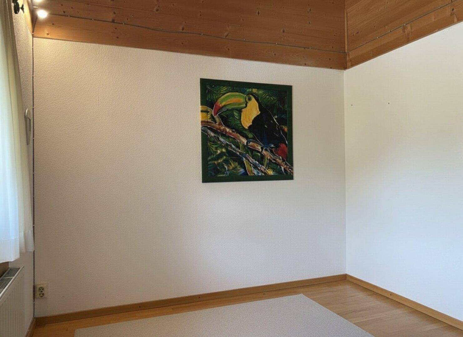 Leerer Raum mit Holzboden, weißen Wänden und einem bunten Wandbild.