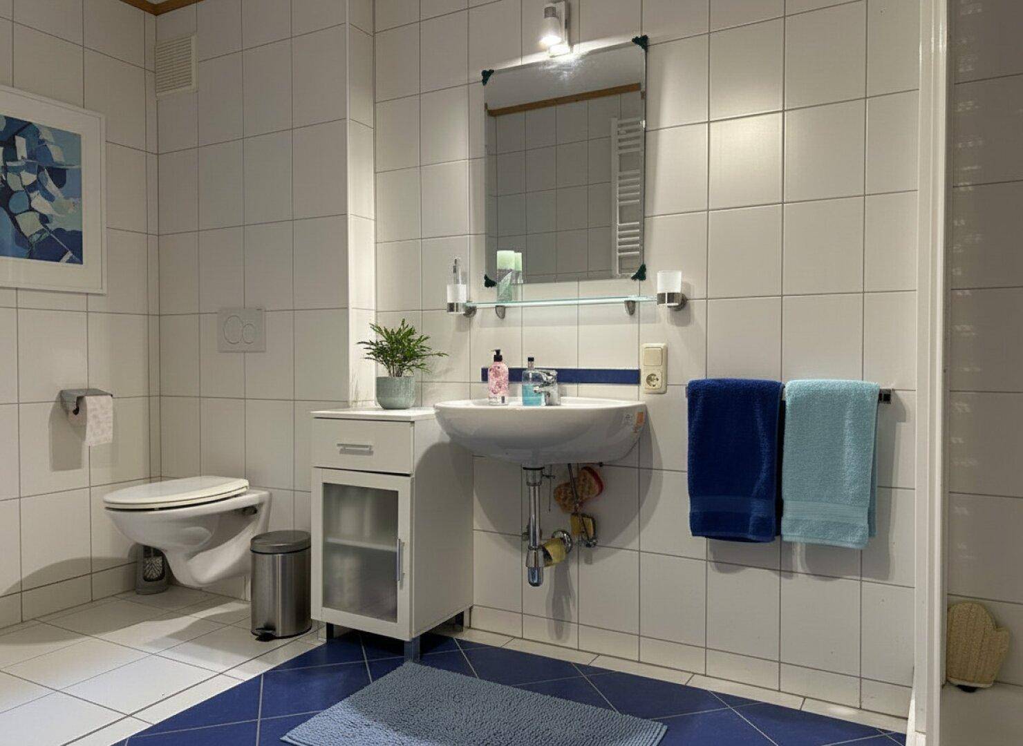 Modernes Badezimmer mit blauen Bodenfliesen, weißer Wandverkleidung und Einzelwaschbecken.
