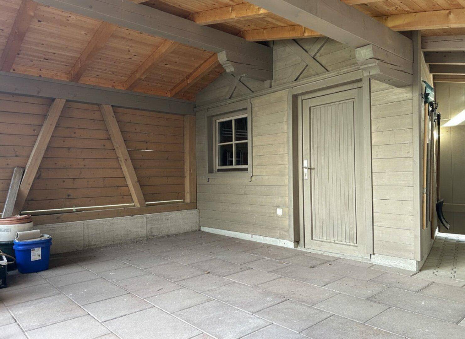 Überdachter Außenbereich mit gepflastertem Boden und Holzwänden, ideal als Abstellfläche.