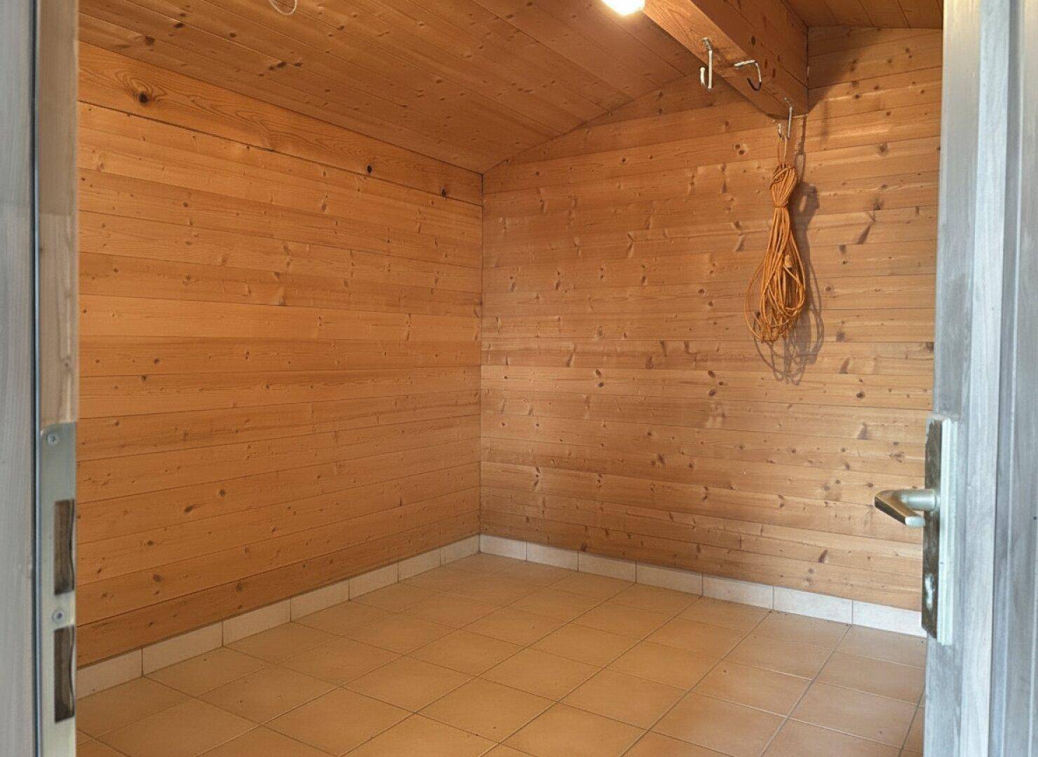 Kleiner Abstellraum mit Holzwänden und Fliesenboden, ideal für Gartengeräte.