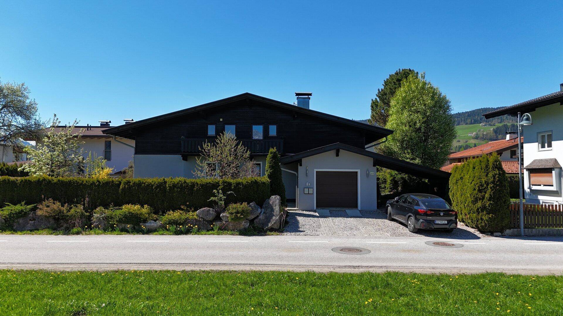Traditionelles Haus im Chalet-Stil mit dunkler Holzfassade, Garage und gepflegtem Vorgarten.