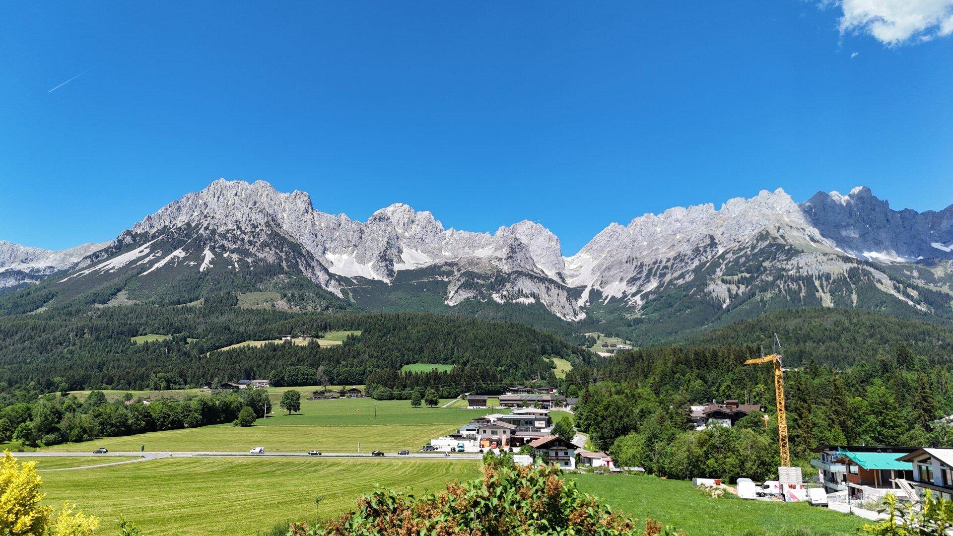 Atemberaubender Blick auf die imposante Bergkette und die umliegende grüne Landschaft mit einigen Gebäuden.