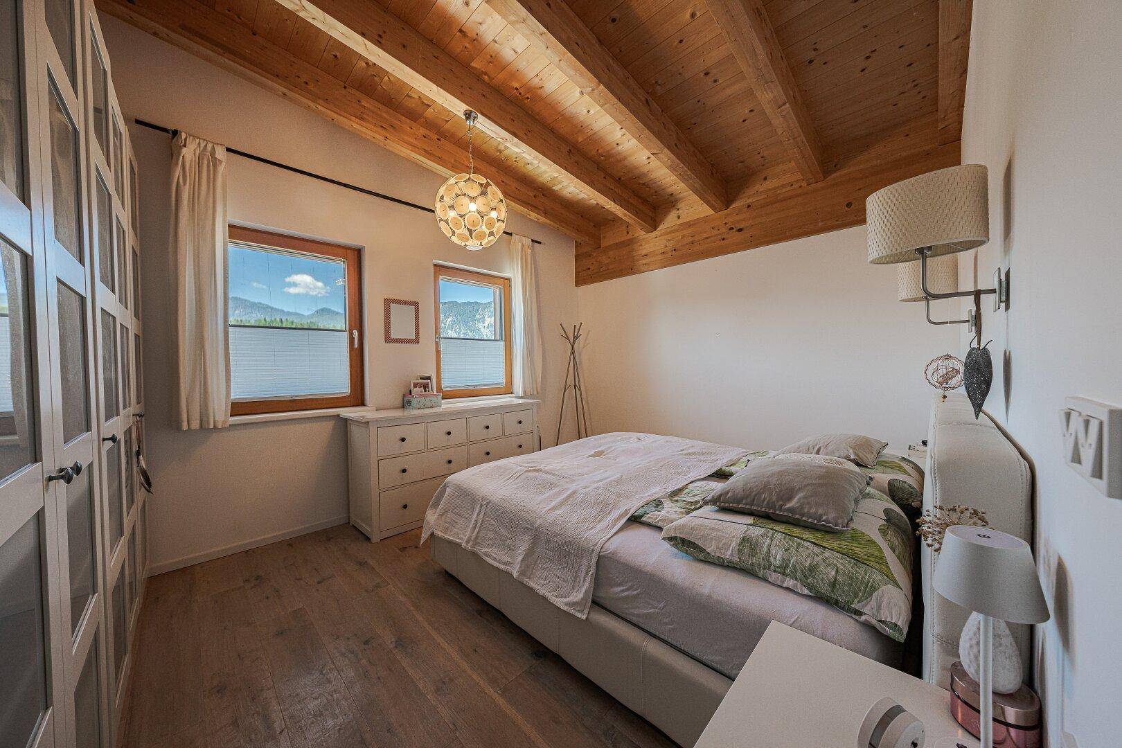 Gemütliches Schlafzimmer mit Holzbalkendecke, Kleiderschrank und Bergblick.