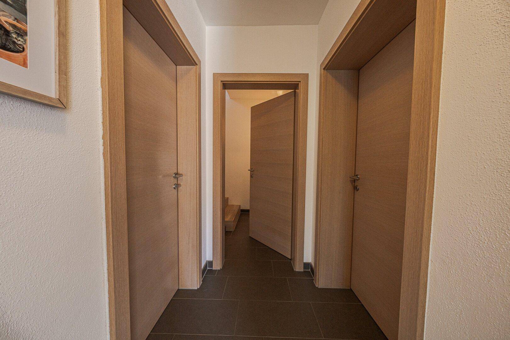 Heller Flur mit Holztüren und dunklem Fliesenboden, der zu verschiedenen Zimmern führt.
