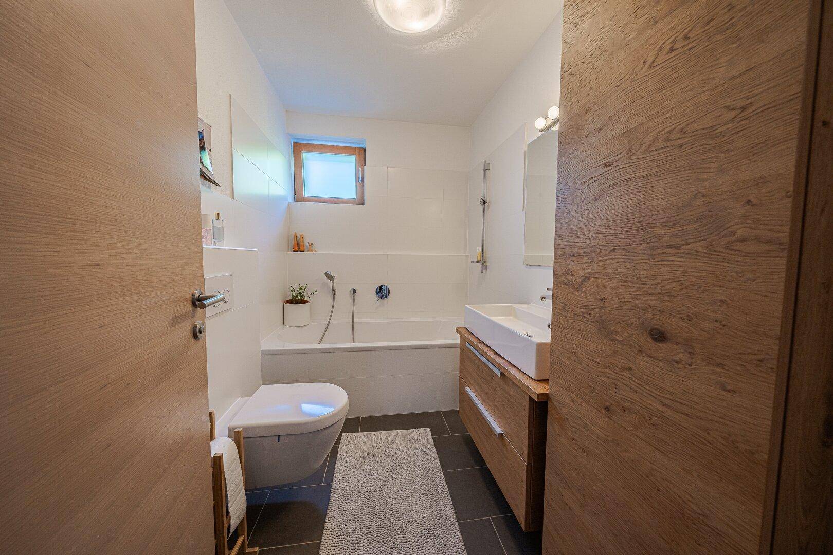 Modernes Badezimmer mit Badewanne, Waschbecken und Fenster für Tageslicht.