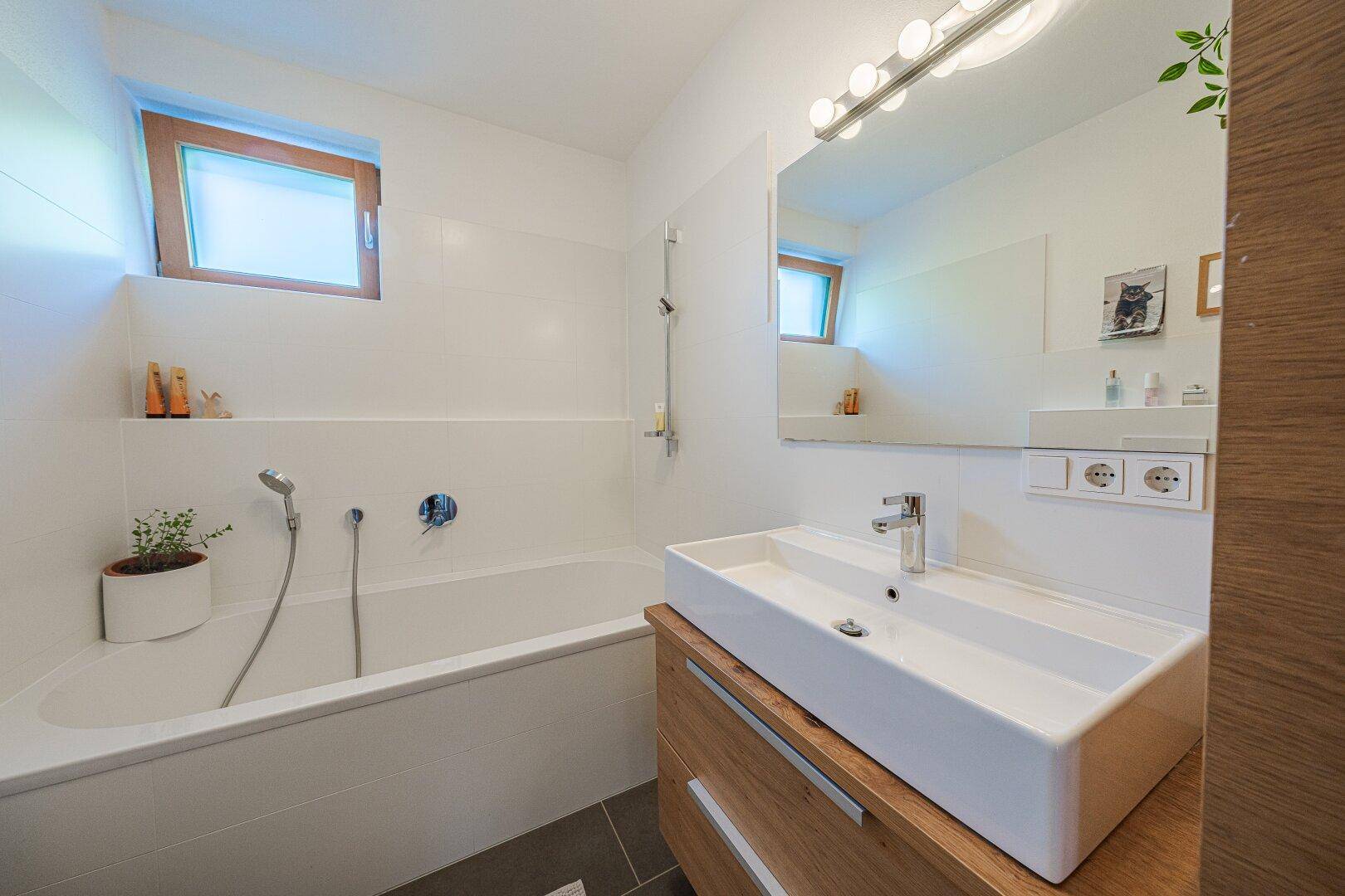Helles Badezimmer mit Badewanne, modernem Waschtisch und großem Spiegel.