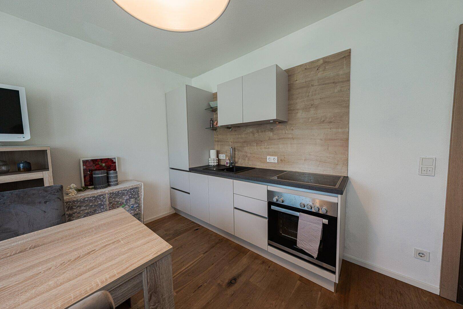 Kompakte Küchenzeile mit Kochfeld, Backofen und Kühlschrank in hellem Design.