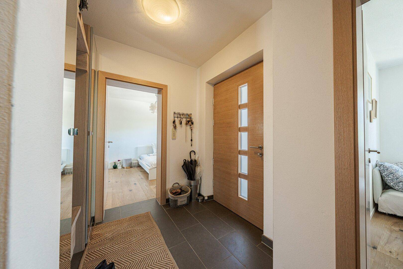 Eingangsbereich mit Garderobe, dunklem Fliesenboden und Holztür.