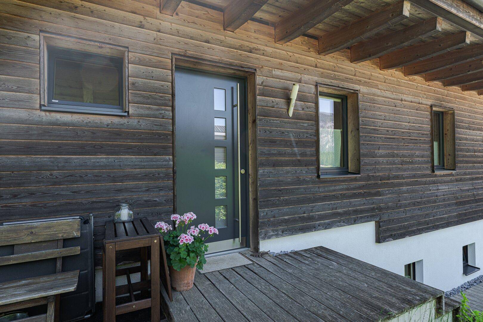 Hauseingang mit Holzwandverkleidung, Holzboden und Blumentopf.