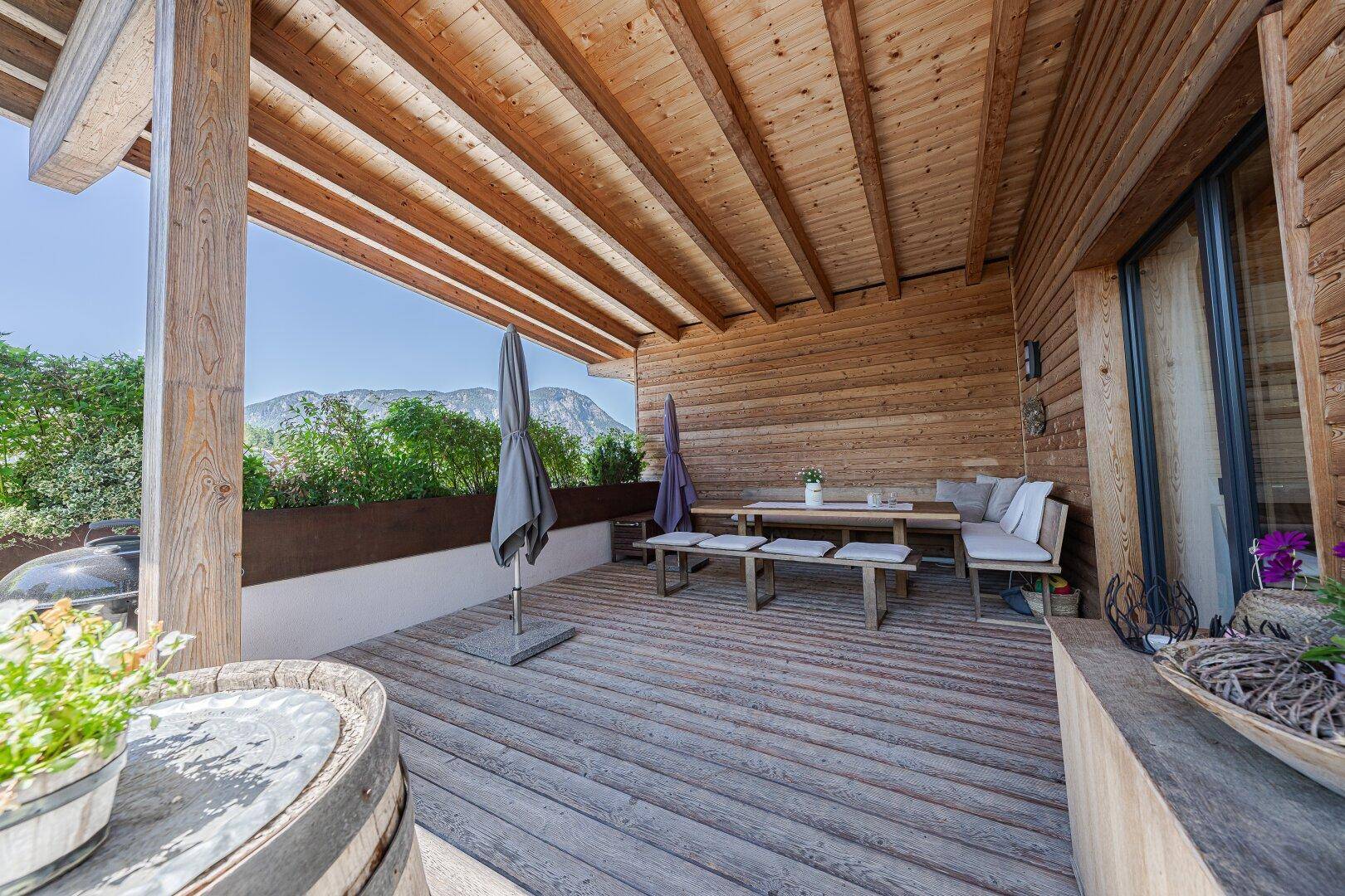 Überdachte Holzterrasse mit Esstisch, Sitzbank und Bergblick.