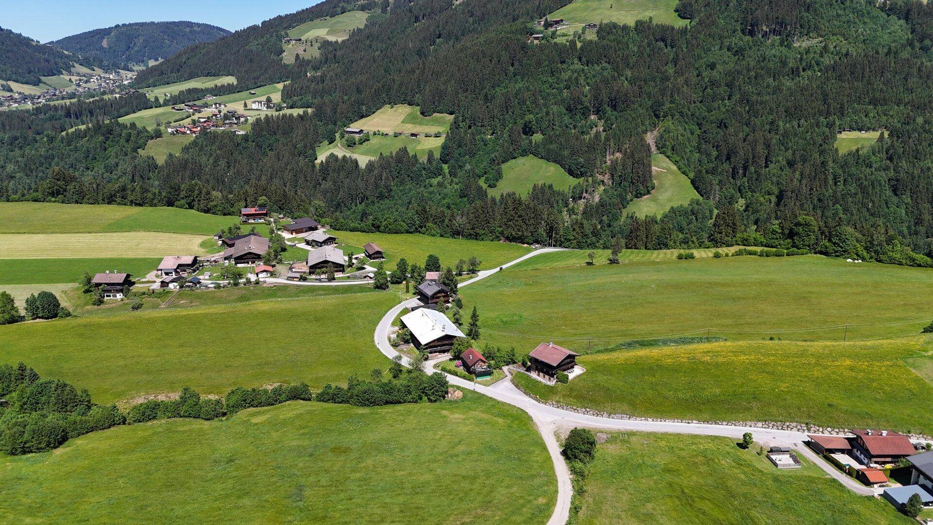 Weitläufige Ansicht einer ländlichen Siedlung eingebettet in grüne Hügel und bewaldete Berge.