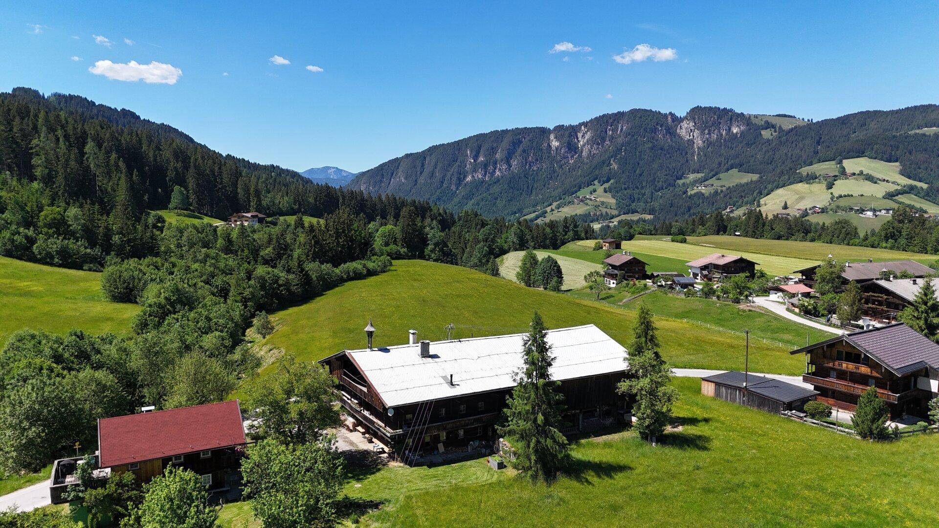 Idyllische Berglandschaft mit verstreuten Häusern, umgeben von üppigen grünen Feldern und dichten Wäldern.
