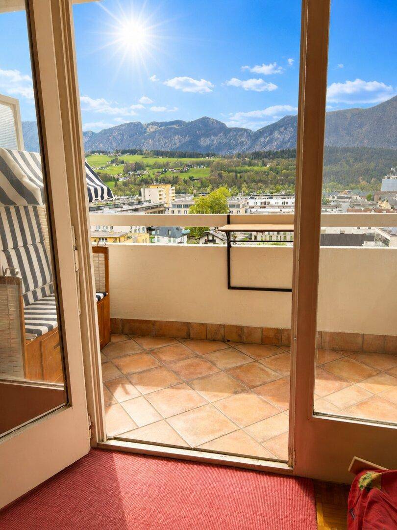 Sonniger Balkon mit Terrakottafliesen und Panoramablick auf die Berge, zugänglich durch eine Glastür.