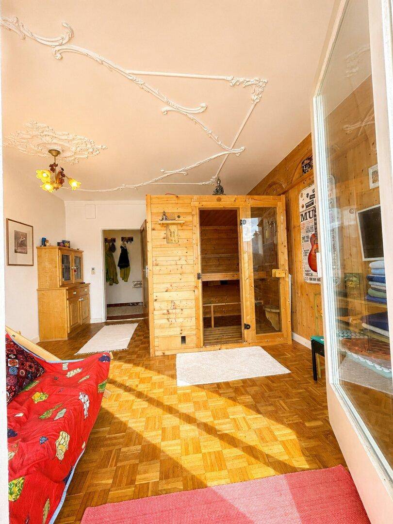 Wellnessbereich mit Sauna, Parkettboden und Zugang zu einem sonnigen Balkon.