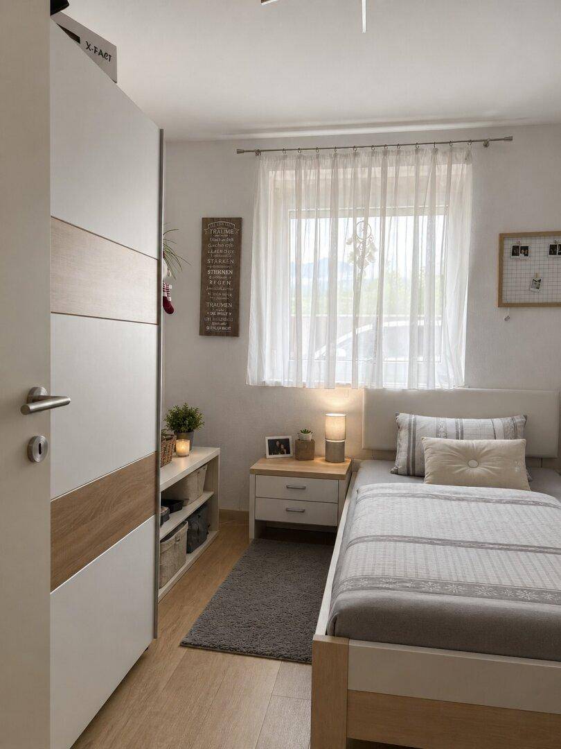 Helles Schlafzimmer mit Einzelbett, Kleiderschrank und Fenster mit Vorhängen.