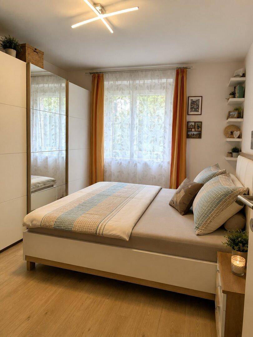 Helles Schlafzimmer mit Doppelbett, Spiegelschrank und farbigen Vorhängen.