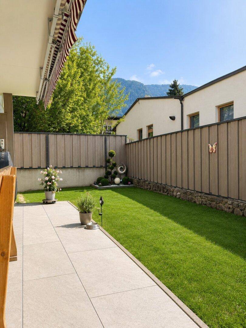 Sonnige Terrasse mit Gartenmöbeln, gepflegtem Rasen und Bergblick im Hintergrund.