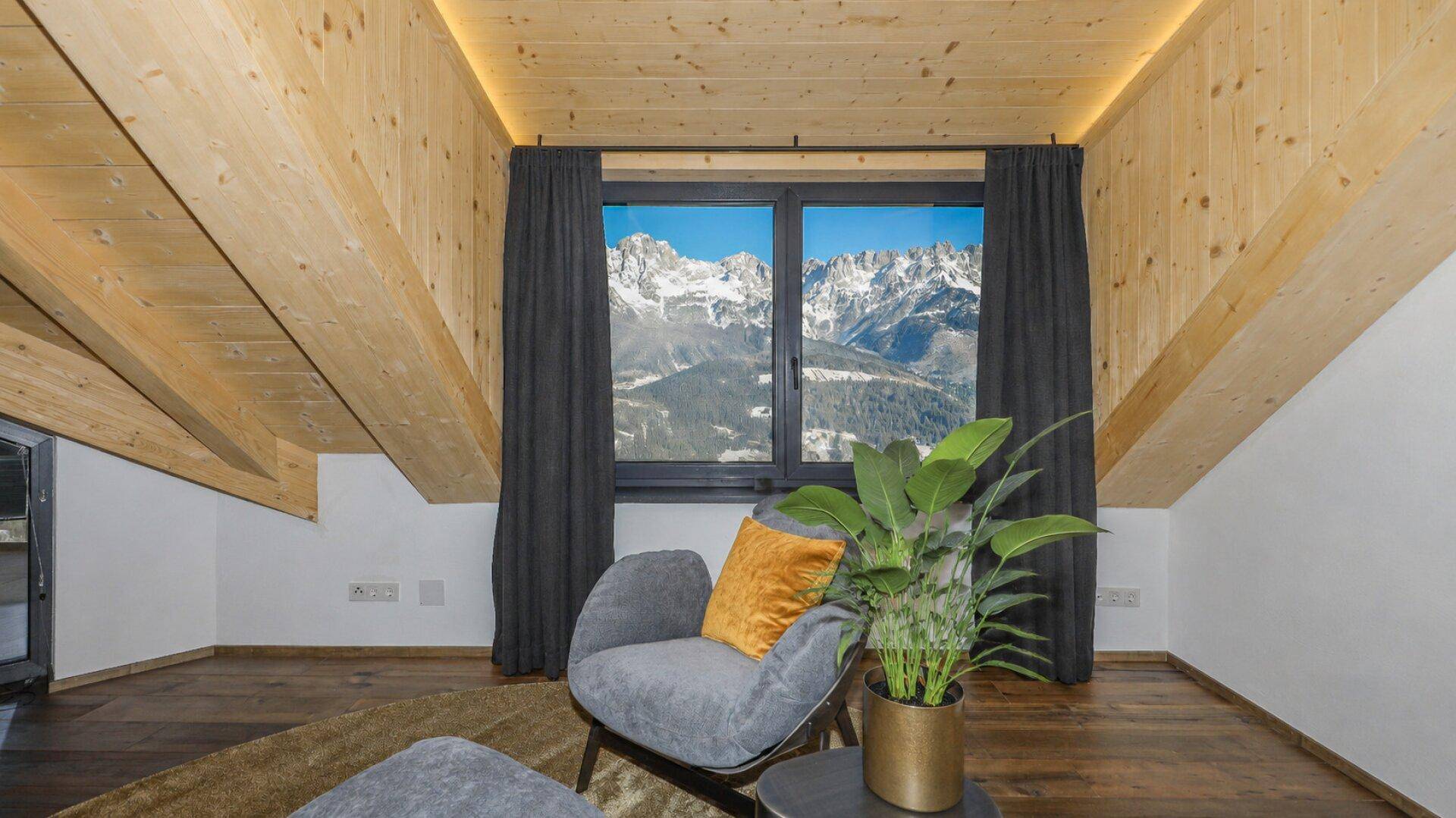 Dachgeschosszimmer mit sichtbaren Holzbalken, gemütlichem Sessel und einem atemberaubenden Bergblick.
