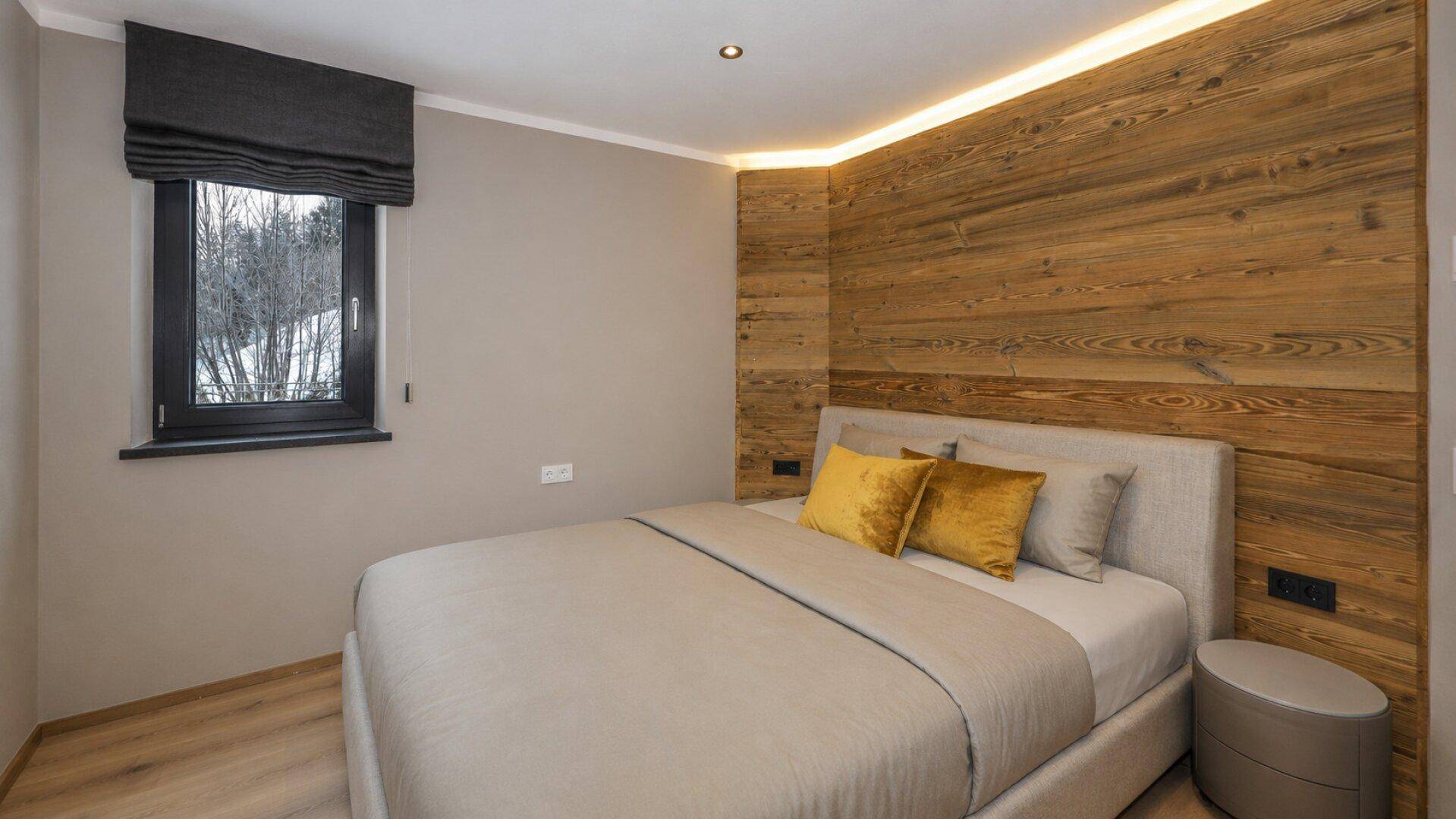 Gemütliches Schlafzimmer mit Holzwandverkleidung und einem Fenster mit Blick auf verschneite Bäume.