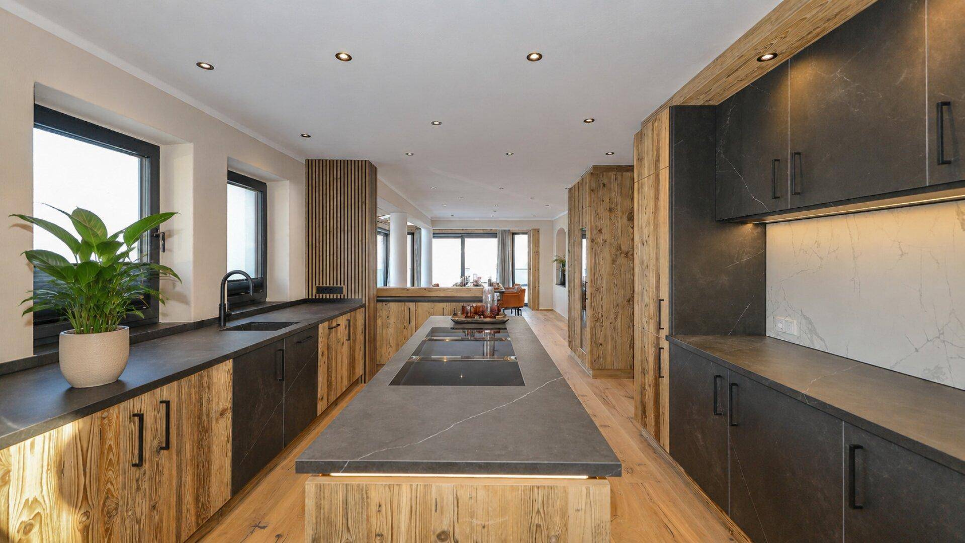 Moderne Küche mit Holzelementen, dunklen Arbeitsplatten und einer Kochinsel in einem offenen Wohnbereich.
