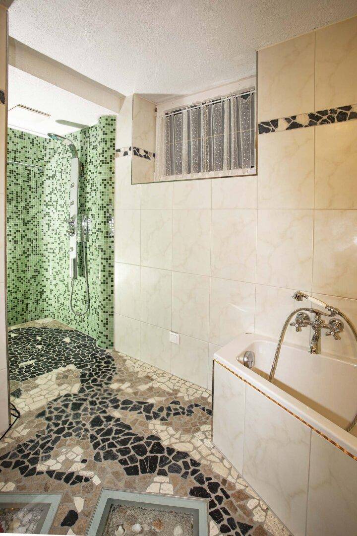 Badezimmer mit Badewanne, Duschbereich und auffälligem Mosaikboden.