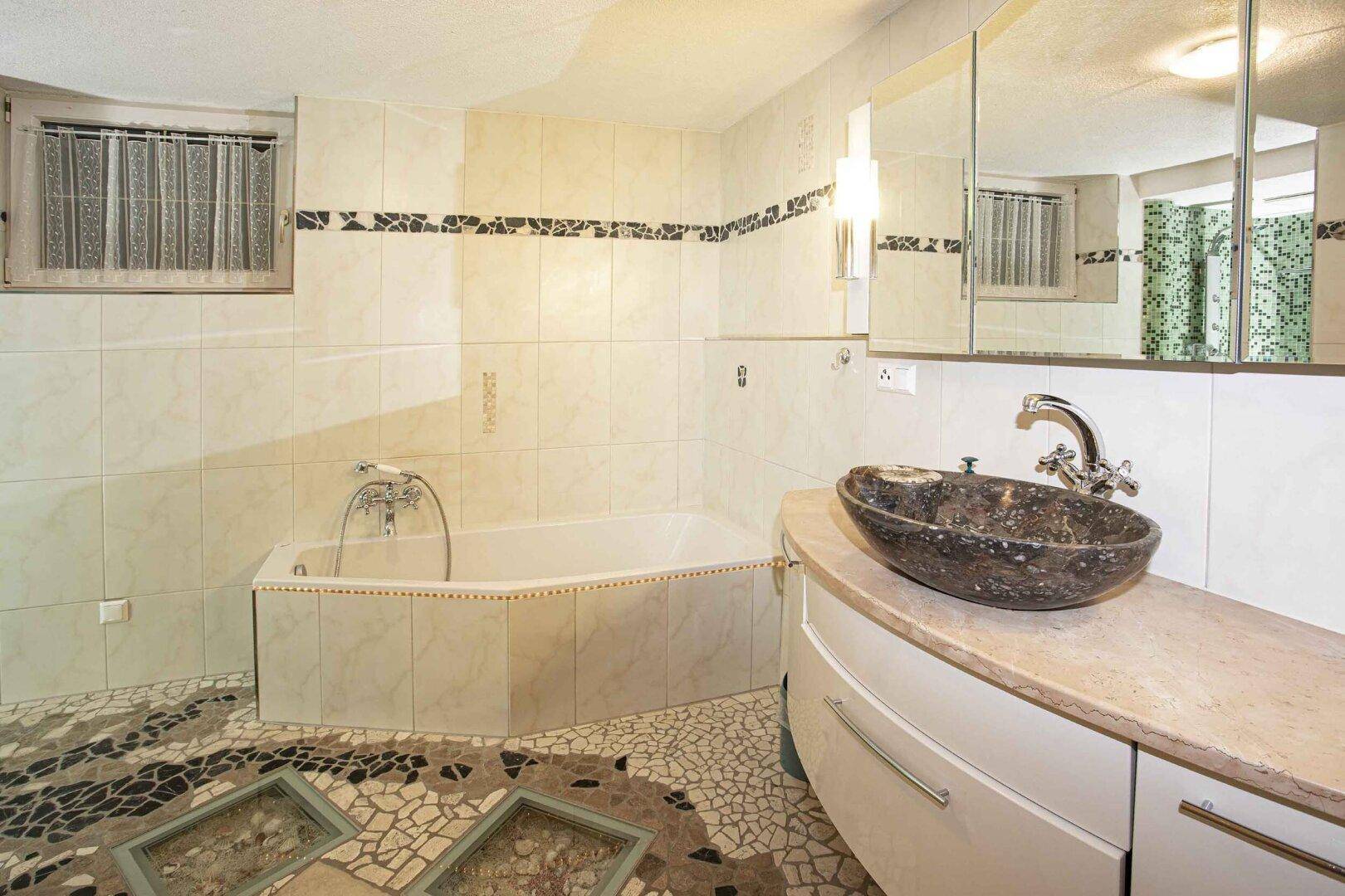 Geräumiges Badezimmer mit Badewanne, einzigartigem Mosaikboden und Steinwaschbecken.