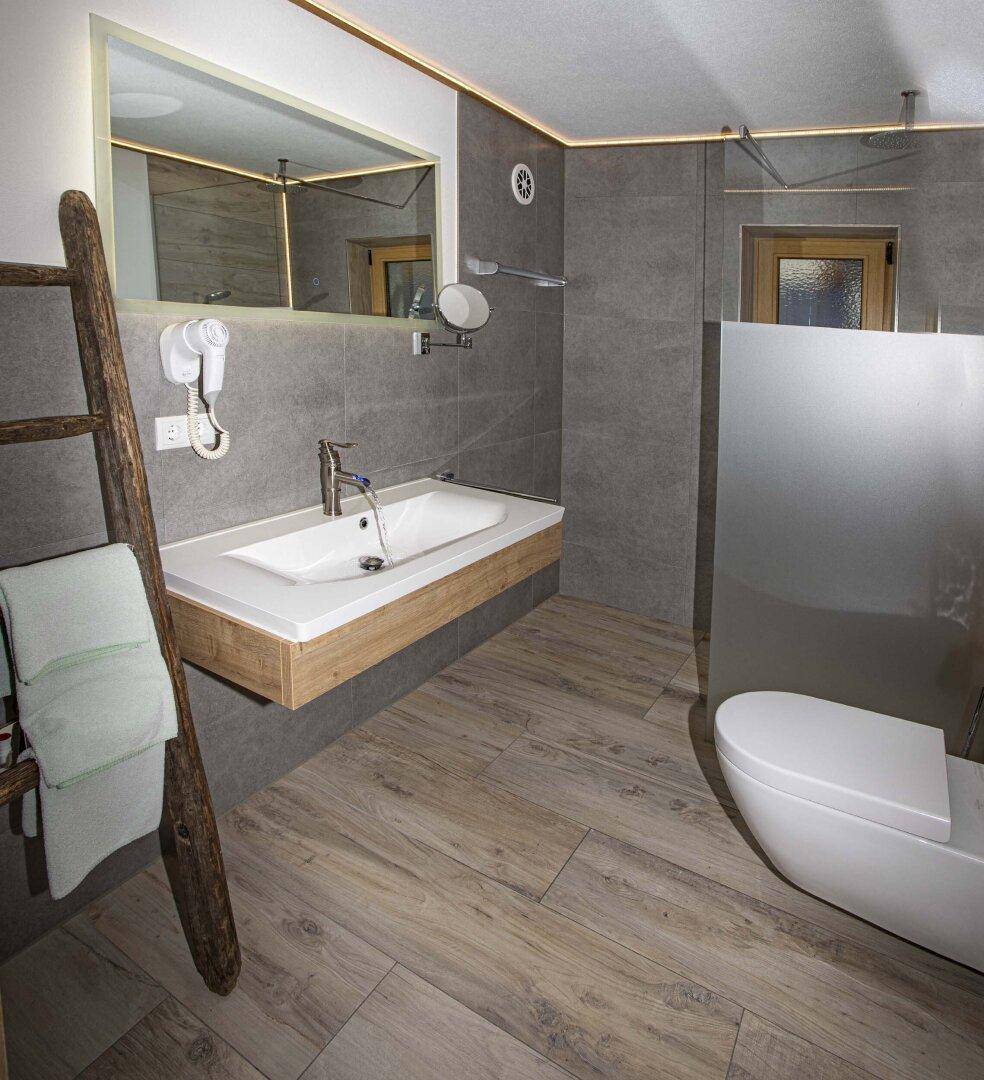 Modernes Badezimmer mit schwebendem Waschbecken, Toilette und begehbarer Dusche.