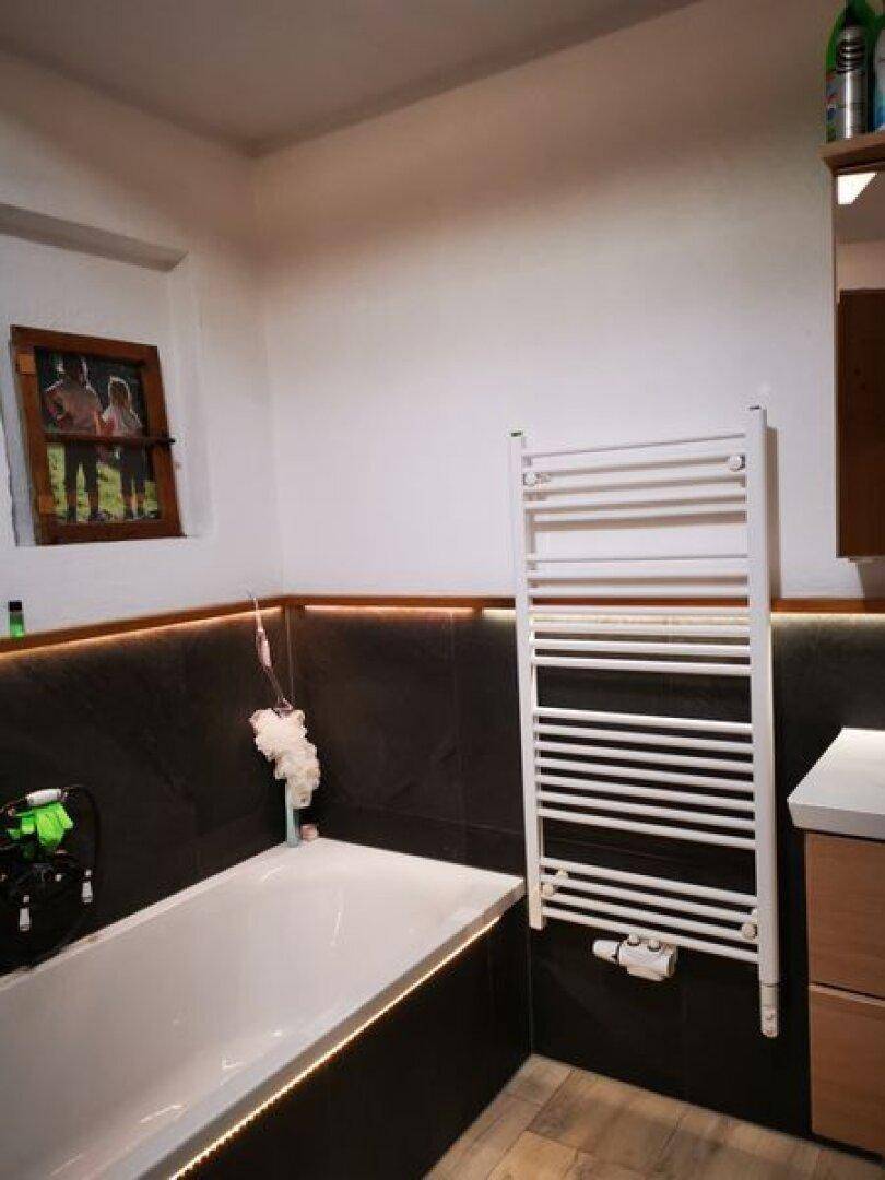 Badezimmer mit Badewanne, beheiztem Handtuchhalter und dunklen Fliesen.