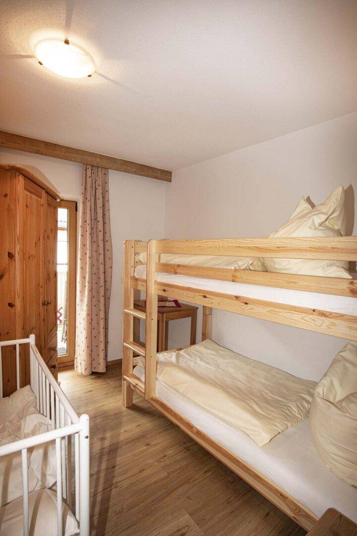 Kinderzimmer mit Etagenbett, Babybett und Holzschrank.