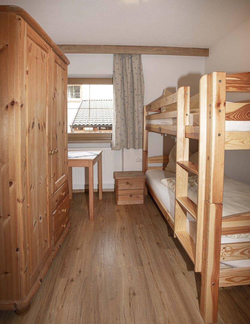 Kinderzimmer mit Etagenbett, Holzschrank und Blick auf das Dach.