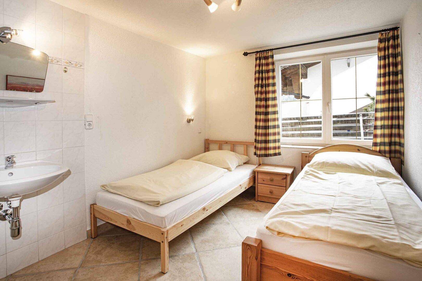 Helles Schlafzimmer mit zwei Einzelbetten, Holzmöbeln und Fliesenboden.