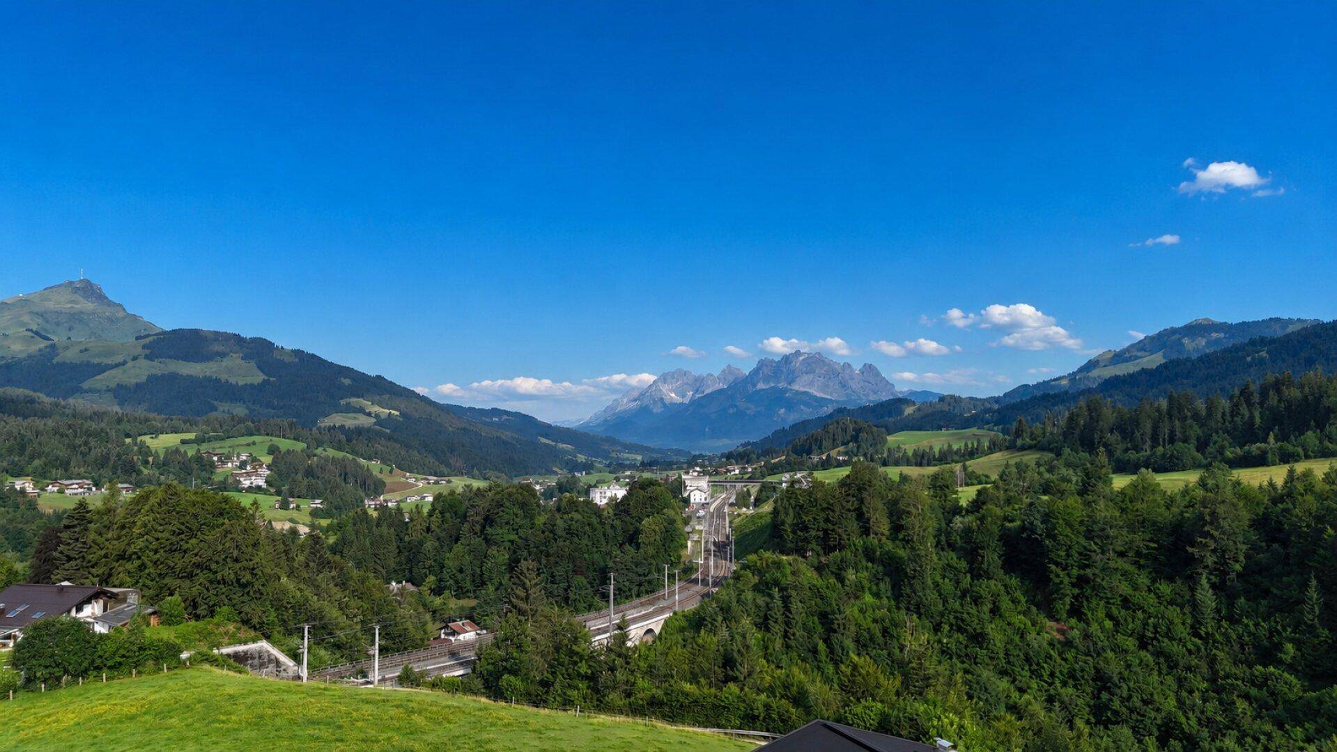 Breiter Ausblick auf eine Berglandschaft mit einer Eisenbahnlinie, die sich durch das Tal schlängelt.