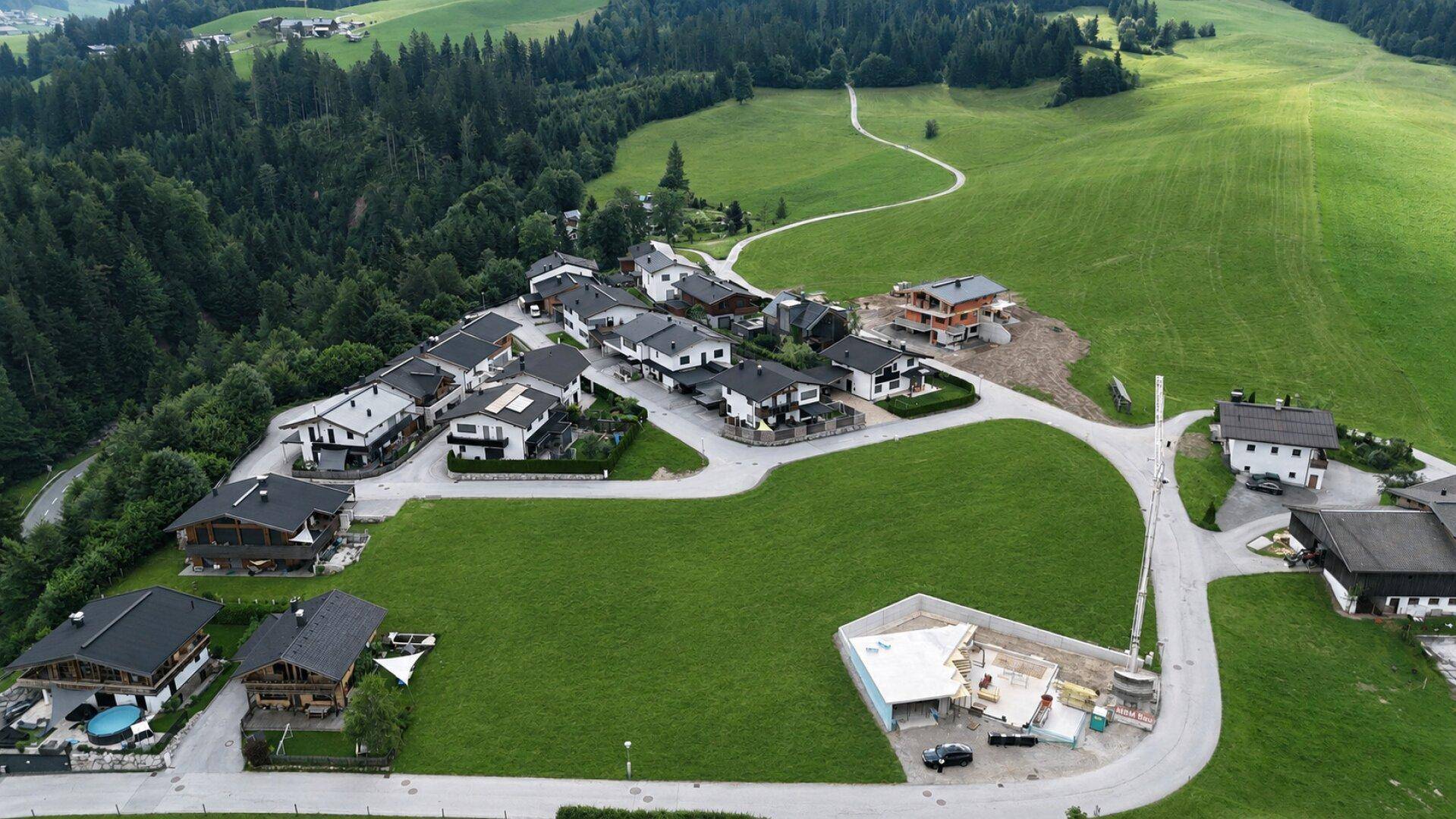 Luftaufnahme einer ländlichen Wohnsiedlung, umgeben von Wäldern und grünen Hügeln.