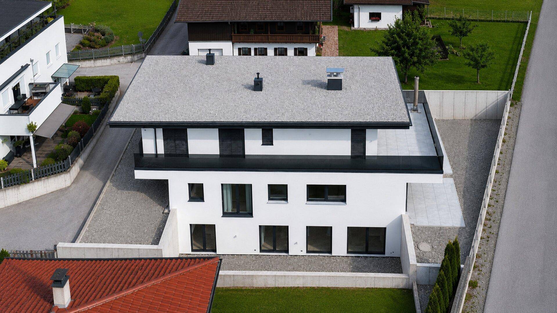 Modernes Einfamilienhaus mit Flachdach, Balkonen und gepflegtem Gartenbereich von oben.