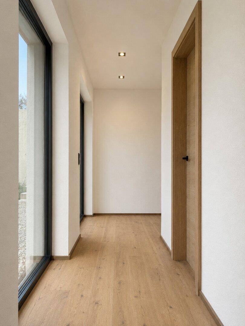 Heller Flur mit Holzboden, Holztür und großen Fenstern, die viel Licht hereinlassen.