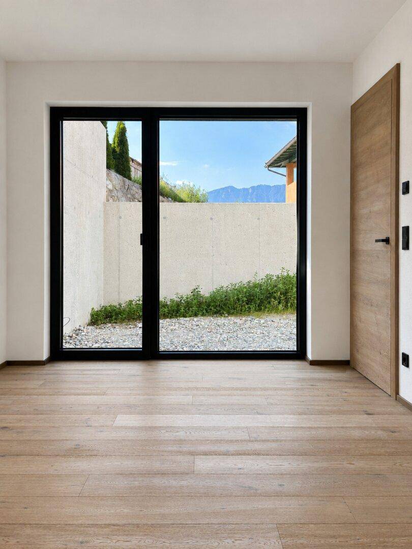 Leeres Zimmer mit Holzboden und großem Fenster mit Bergblick und viel Tageslicht.