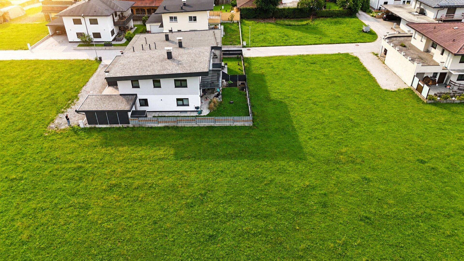 Weitläufige grüne Wiese mit einem modernen Haus im Hintergrund unter strahlendem Sonnenschein.