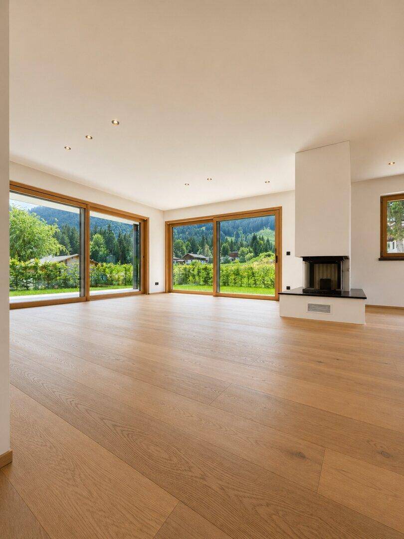 Helles Wohnzimmer mit Eichenparkett, großzügigen Fensterfronten und modernem Kamin mit Bergblick.
