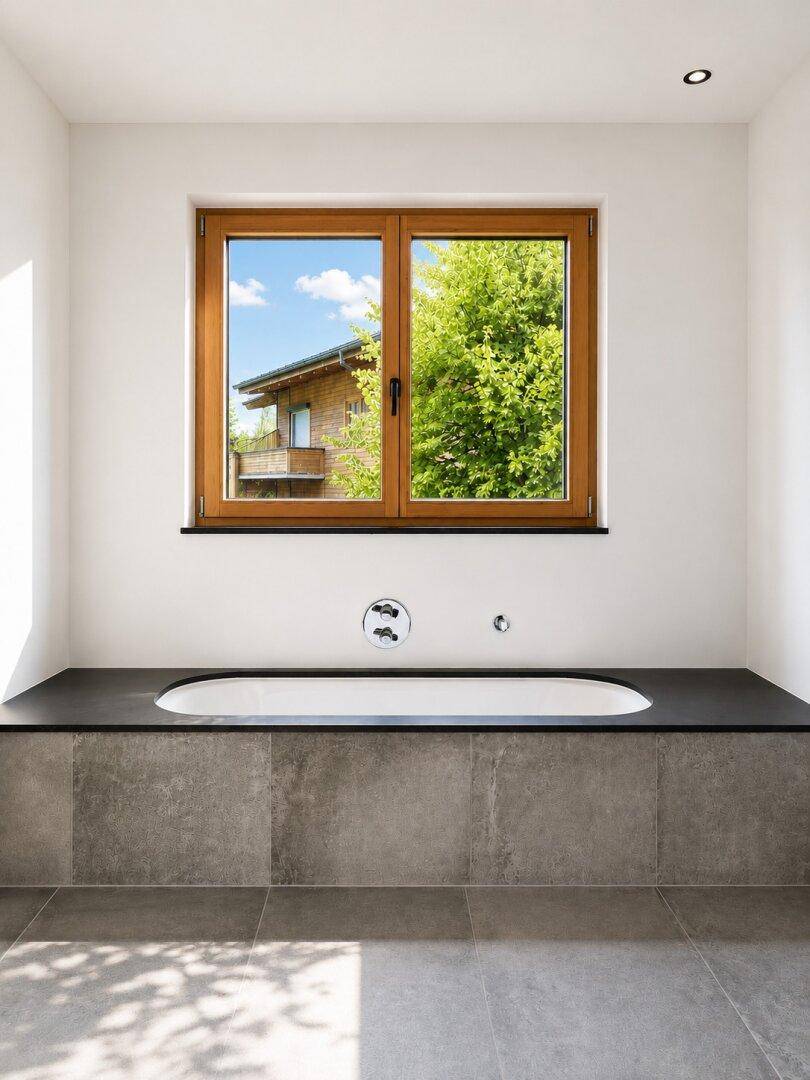 Helles Badezimmer mit eingebauter Badewanne unter einem Fenster und Blick ins Grüne.