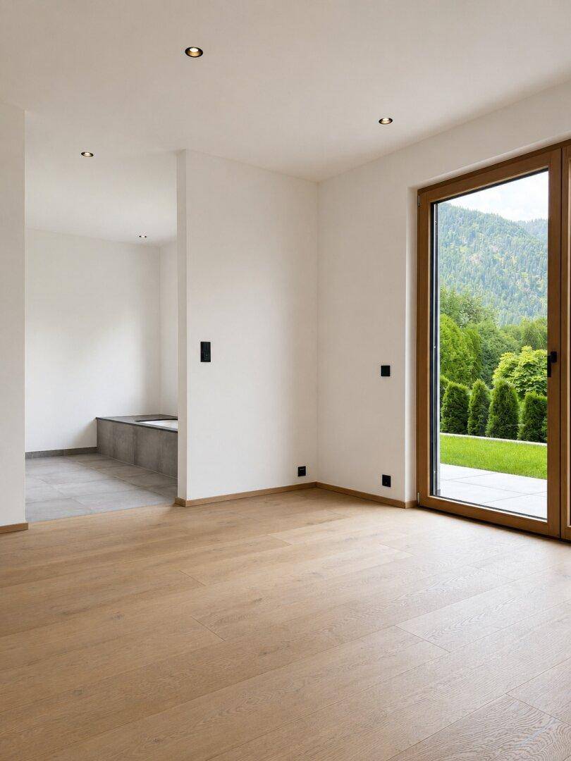 Heller Raum mit Holzboden, großem Fenster und Blick auf die grüne Berglandschaft.