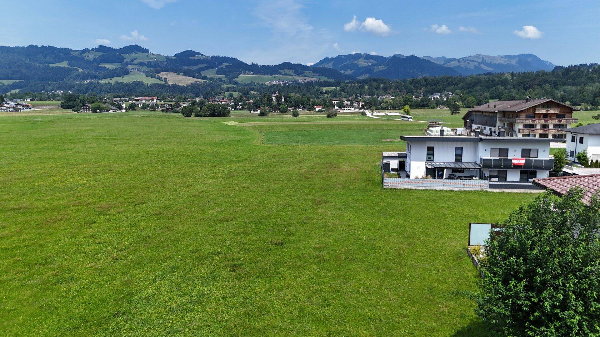 Große Grünfläche umgeben von modernen Wohnhäusern mit Blick auf die hügelige Landschaft.