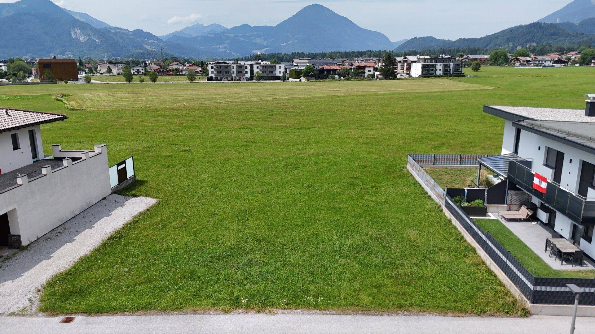 Weitläufige Grünfläche mit Blick auf die umliegende Berglandschaft und Wohnbebauung.