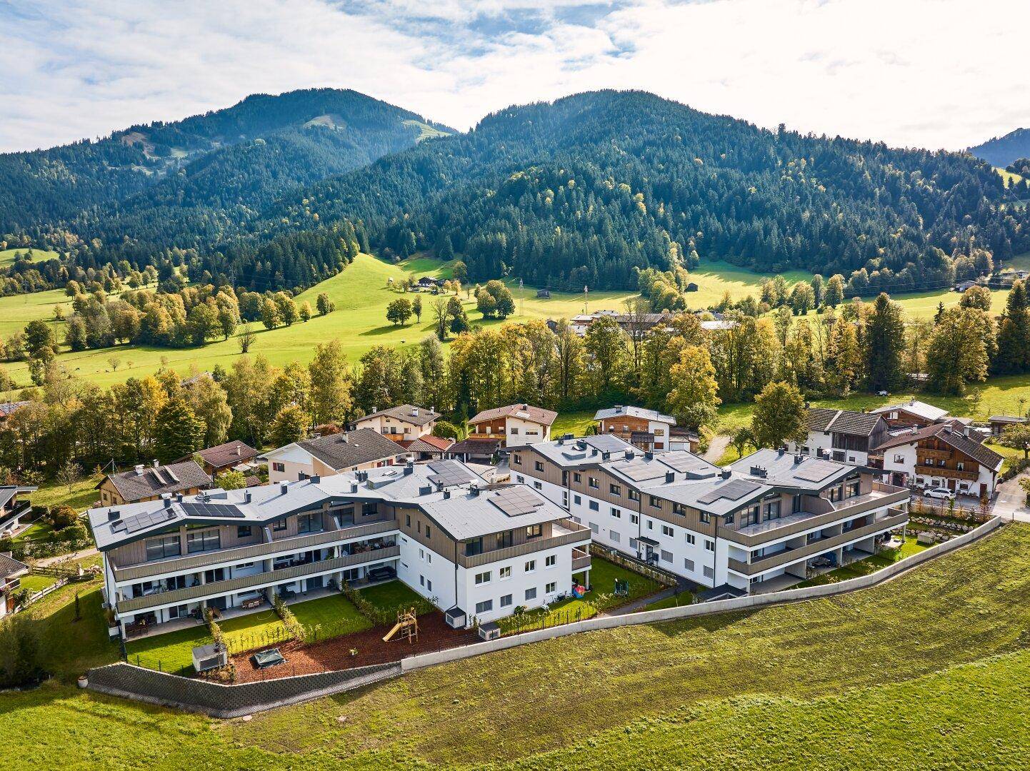 Luftaufnahme einer modernen Wohnanlage eingebettet in eine grüne Berglandschaft.