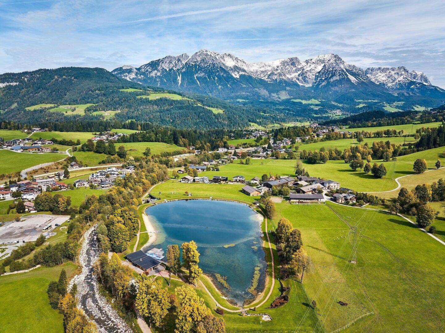 Malerische Luftaufnahme einer Berglandschaft mit See, Dorf und schneebedeckten Gipfeln.