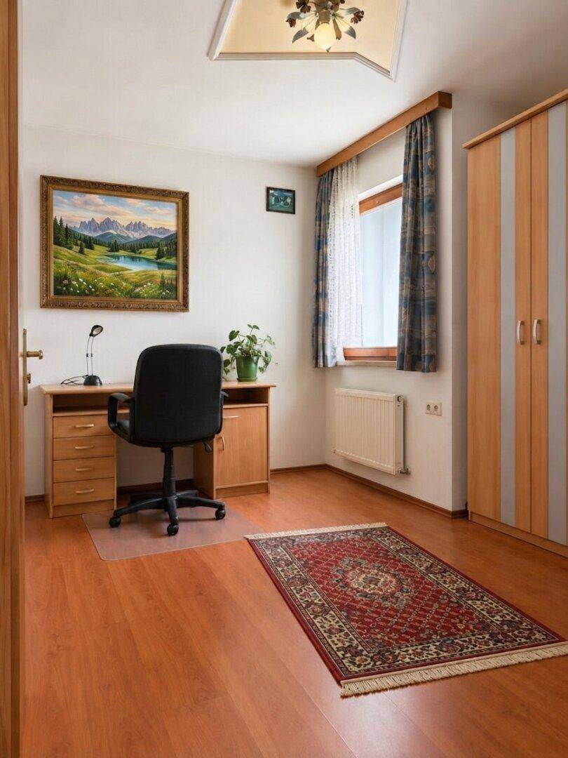 Helles Büro mit Holzschreibtisch, Bürostuhl und Kleiderschrank. Der Raum verfügt über einen warmen Holzboden und ein Fenster.