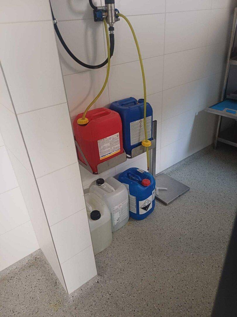 Verschiedene Plastikbehälter mit Flüssigkeiten auf einem Regal in einem Lager- oder Reinigungsbereich.